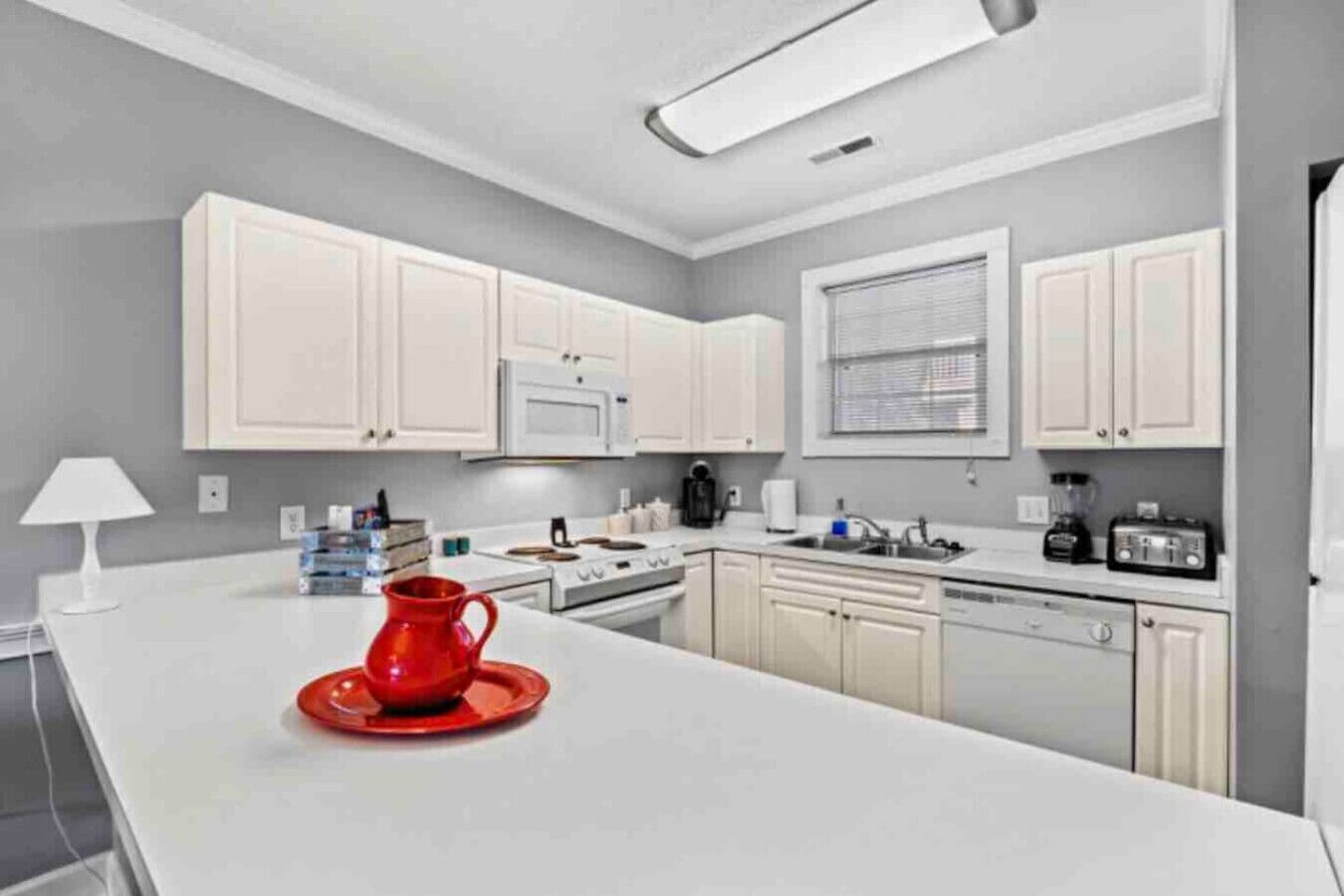 A modern kitchen with white cabinets, a red cup on the counter, and a white lamp.