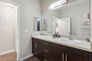 Un baño moderno con dos lavamanos, armarios de madera oscura y un espejo grande.