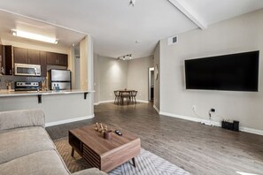A modern living room with a flat-screen TV, a dining area, and a kitchen with a microwave and stove. - Chic Marina Oasis 5 Star Amenities Central (Marina del Rey)