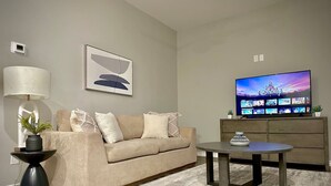 Ein Wohnzimmer mit beiger Couch, Couchtisch, Fernseher auf Holzständer und einem gemusterten Teppich.