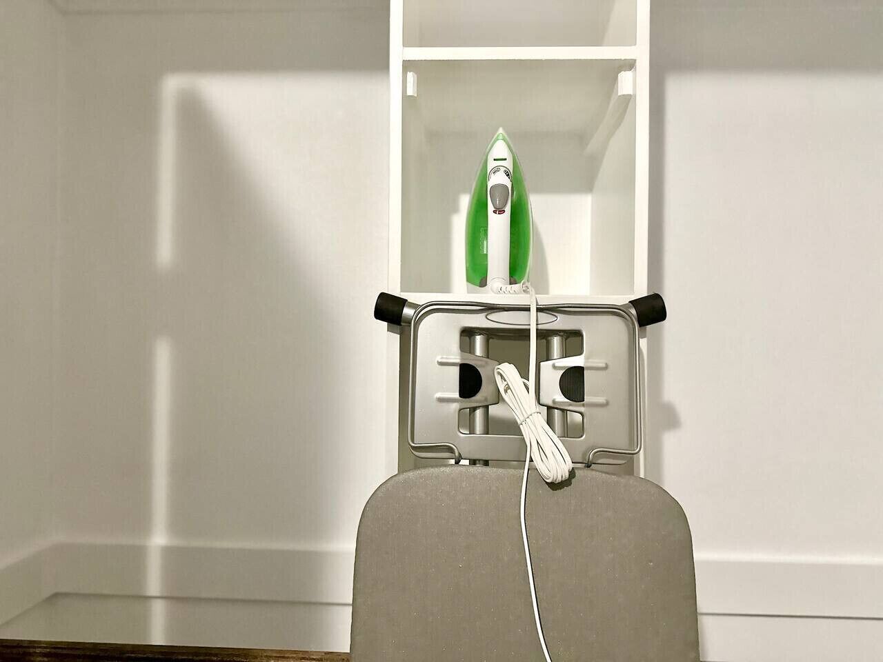 A room with a white wall and a shelf containing a green and white iron.