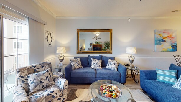 Un salon moderne avec un canapé bleu, des fauteuils à motifs, une table basse en verre et deux lampadaires.