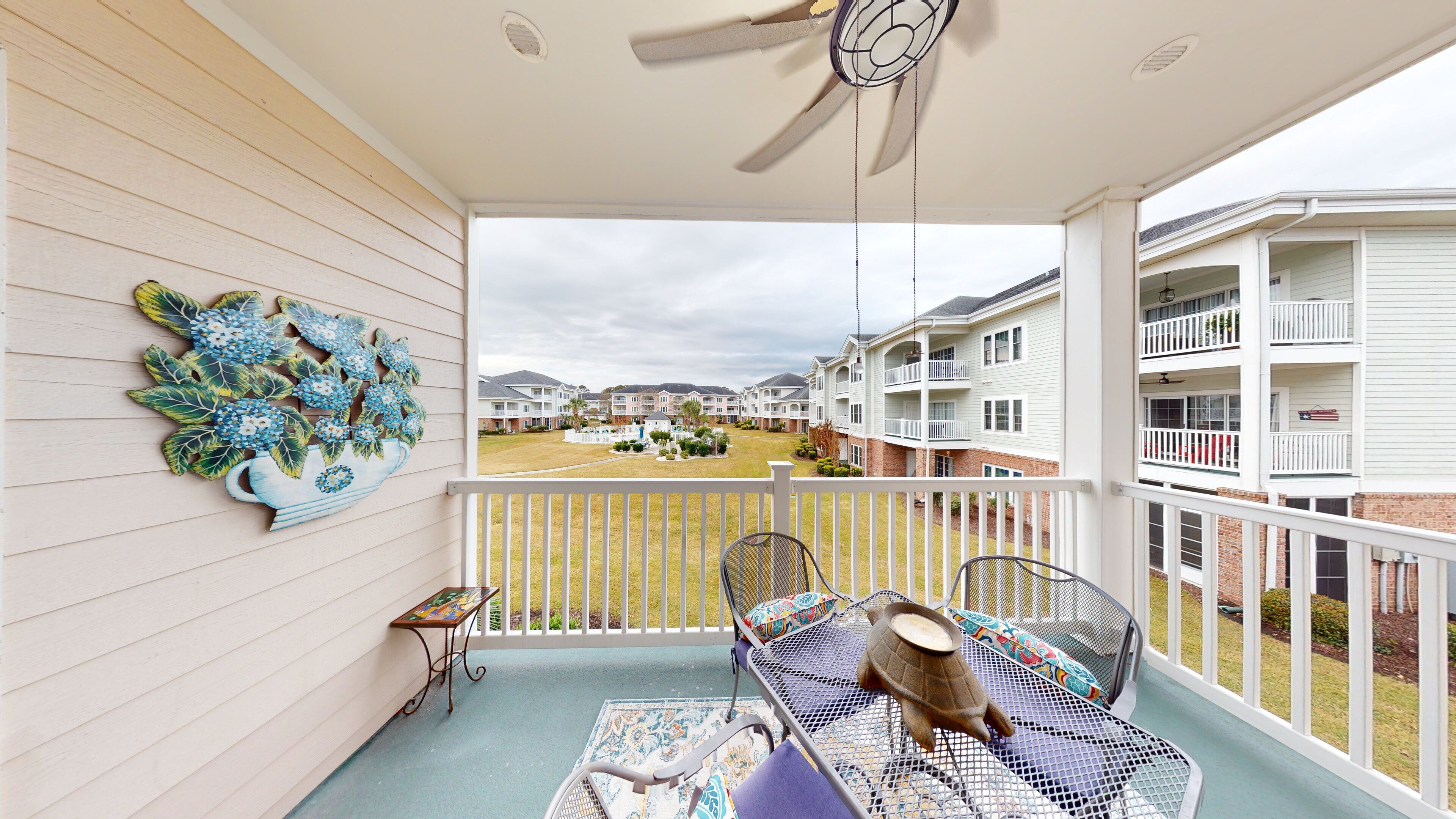 A covered balcony with a ceiling fan, a decorative wall piece, and a view of a residential complex.
