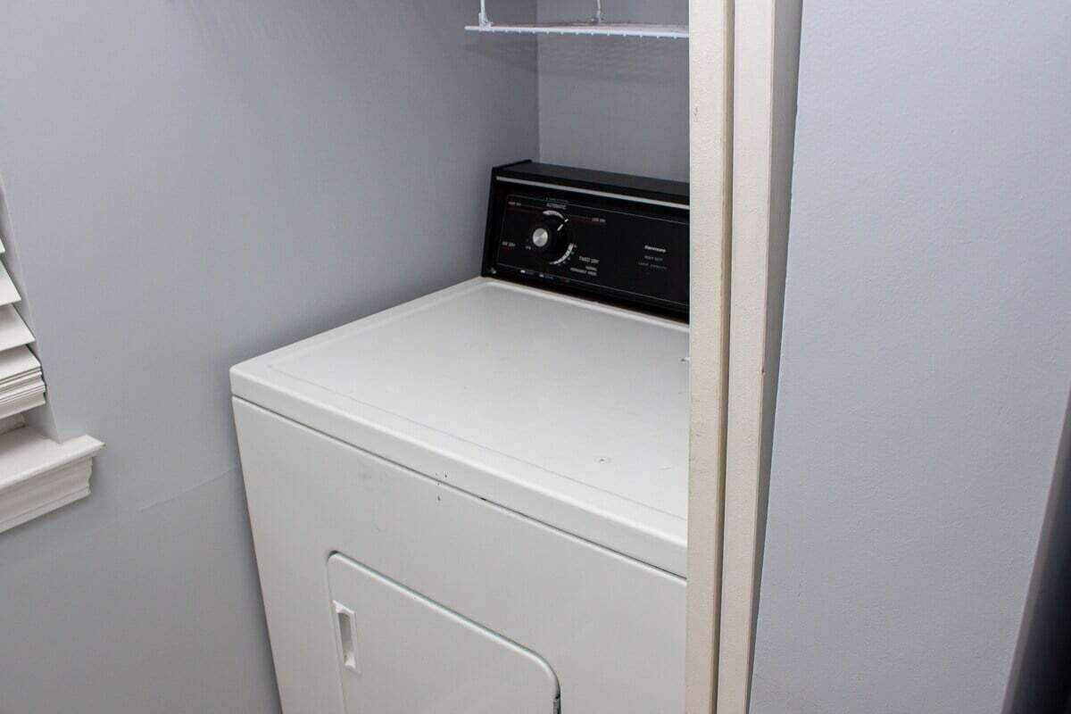 A compact laundry room with a white washer and dryer, a small shelf, and a door leading to another room.