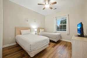A bedroom with two beds, a ceiling fan, a window with curtains, and a TV on a cabinet. - River Oaks 55E (Myrtle Beach)