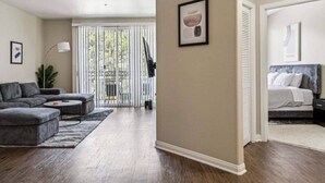 A modern living room with a grey sectional sofa, a small coffee table, and a large window with blinds. - Cozy Marina Hideaway Gym, Pool & Spa Central (Marina del Rey)