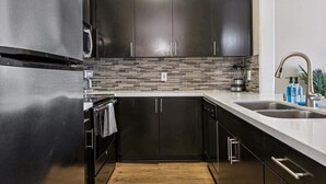 A modern kitchen with dark cabinets, a stainless steel refrigerator, and a tiled backsplash. - Cozy Marina Hideaway Gym, Pool & Spa Central (Marina del Rey)