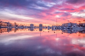 Una marina amb vaixells i edificis reflectits en aigües tranquil·les durant el capvespre.