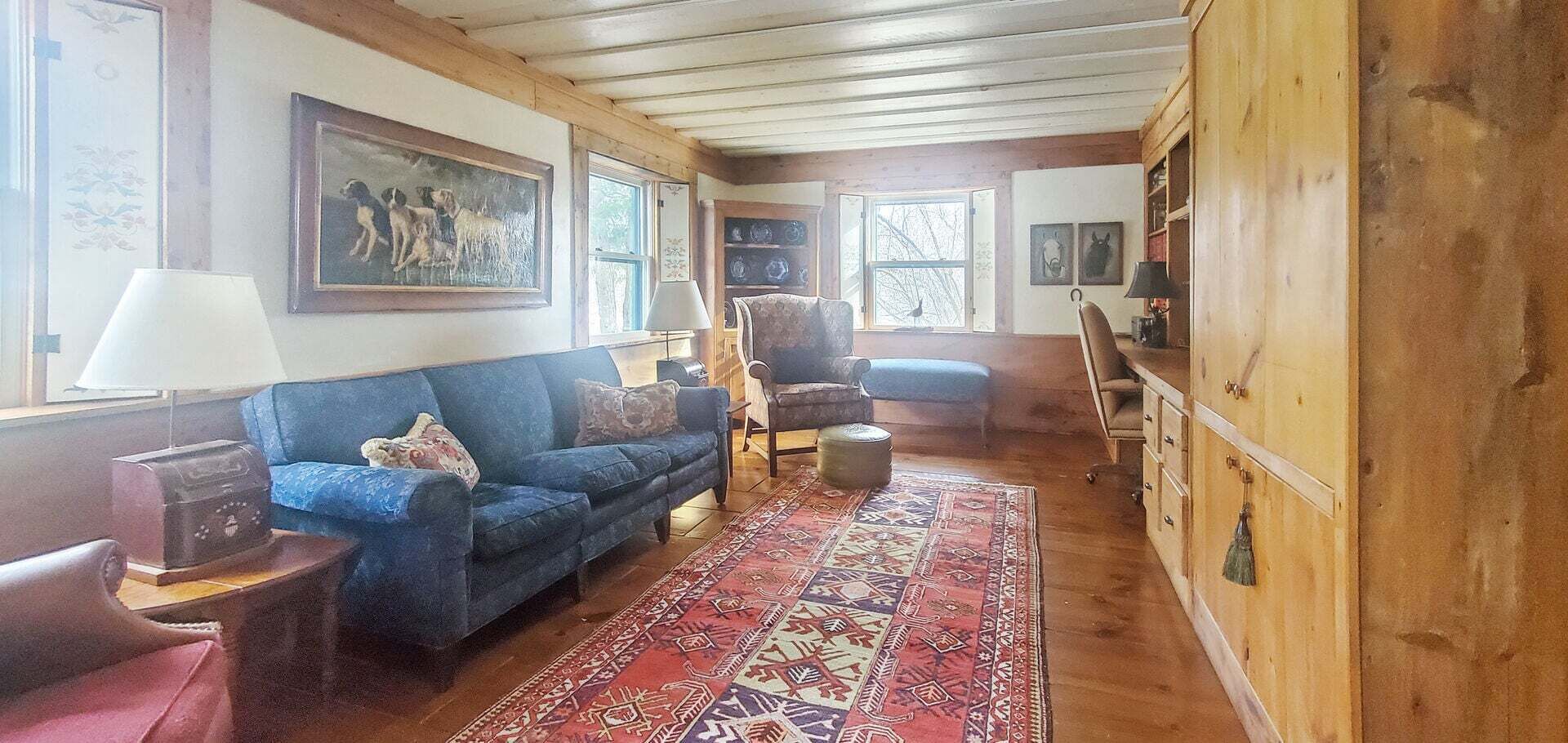A cozy living room with a blue sofa, a patterned rug, and wooden walls.