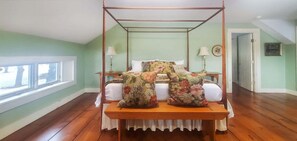 A four-poster canopy bed with floral pillows, a bedside table, and a nightstand in a room with green walls and wooden flooring. - Old Orchard House (Brandon)