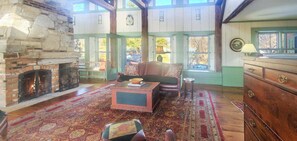 A cozy room with a stone fireplace, a sofa, a wooden dresser, and a large window. - Old Orchard House (Brandon)