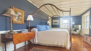 A bedroom with a four-poster bed, a nightstand, a chair, a television, and a window with a view. - Old Orchard House (Brandon)