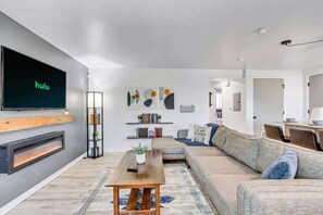 A modern living room with a flat-screen TV, a fireplace, a sofa, a coffee table, and a bookshelf. - Comfortable 2BR Apt Near Capitol Hill & SLC (Salt Lake City)