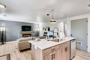 A modern kitchen with a built-in island, a dining area with a sofa, and a flat-screen TV mounted on the wall. - Comfortable 2BR Apt Near Capitol Hill & SLC (Salt Lake City)