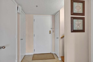 Un couloir avec une porte blanche, un paillasson et deux tableaux encadrés accrochés au mur.