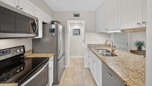 A modern kitchen with white cabinets, a stainless steel refrigerator, a built-in microwave, and a granite countertop. - Ocean Bridge 1A2 (Myrtle Beach)