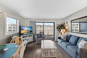 En stue med TV, sofa, lænestol, sofabord og en balkon med udsigt til bygninger.