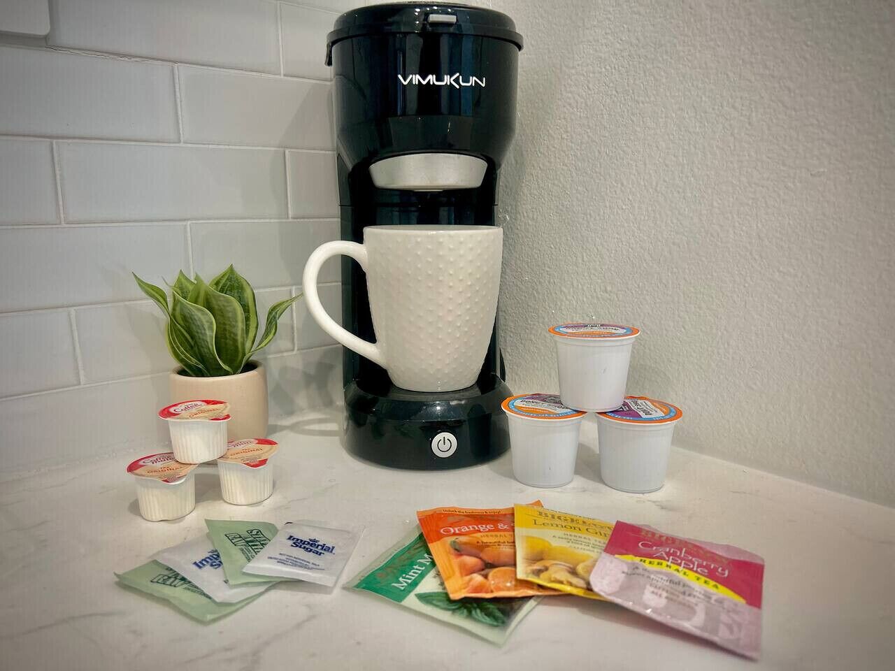 A coffee maker, a white mug, and various tea bags and packets on a countertop.