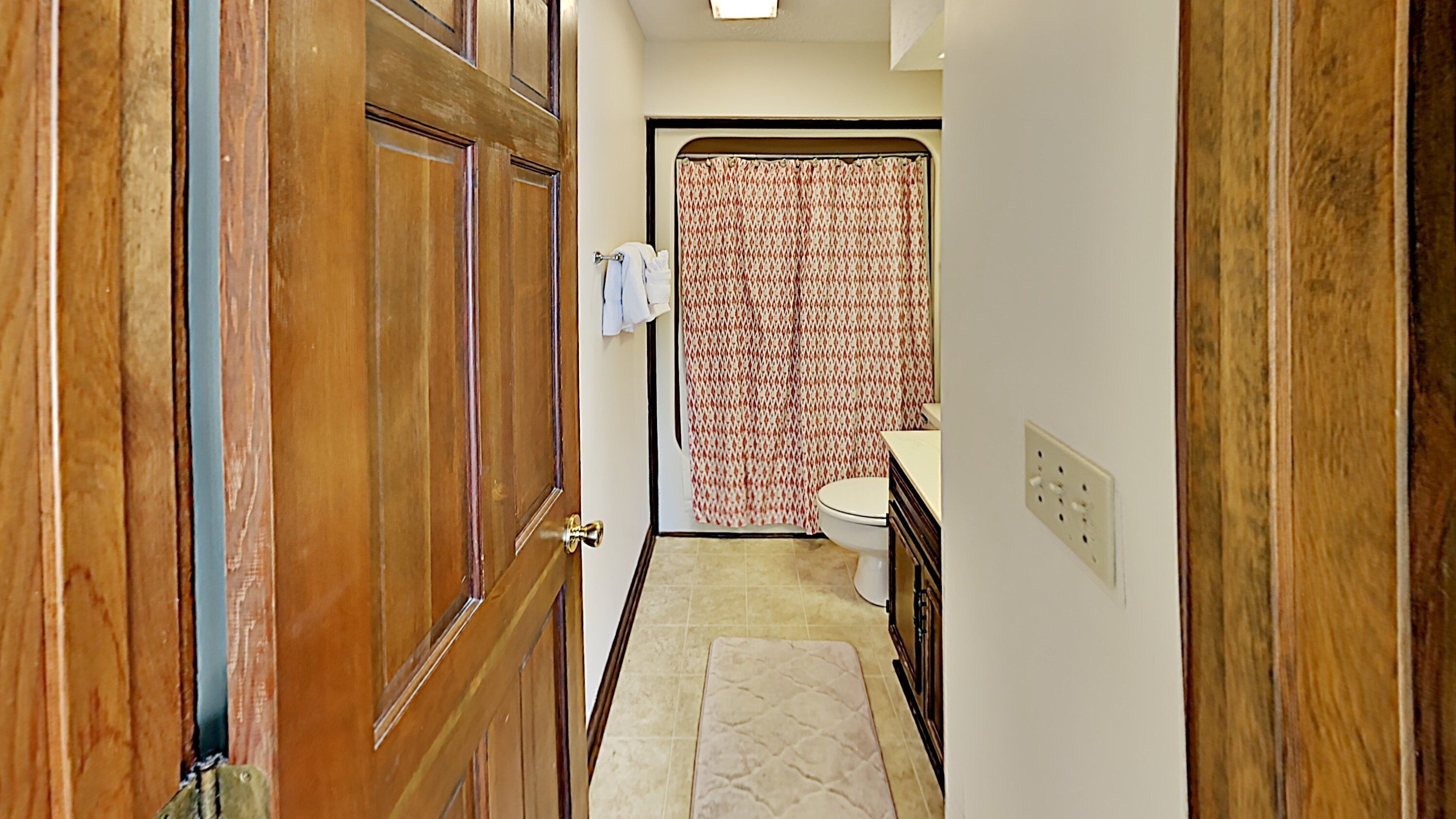 A narrow hallway leading to a bathroom with a toilet and a shower curtain.