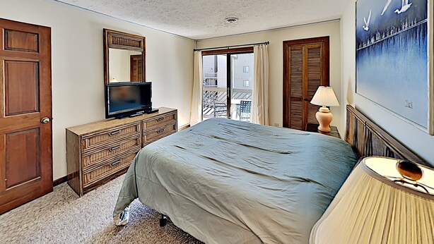 A hotel room with a bed, dresser, television, lamp, and a painting on the wall. - Shipwatch Pointe I F217 (Myrtle Beach)