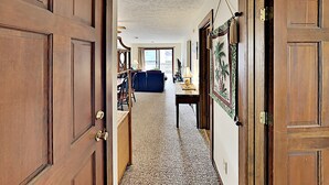 A hallway with wooden doors, a patterned carpet, a blue sofa, and a table with a lamp. - Shipwatch Pointe I F217 (Myrtle Beach)