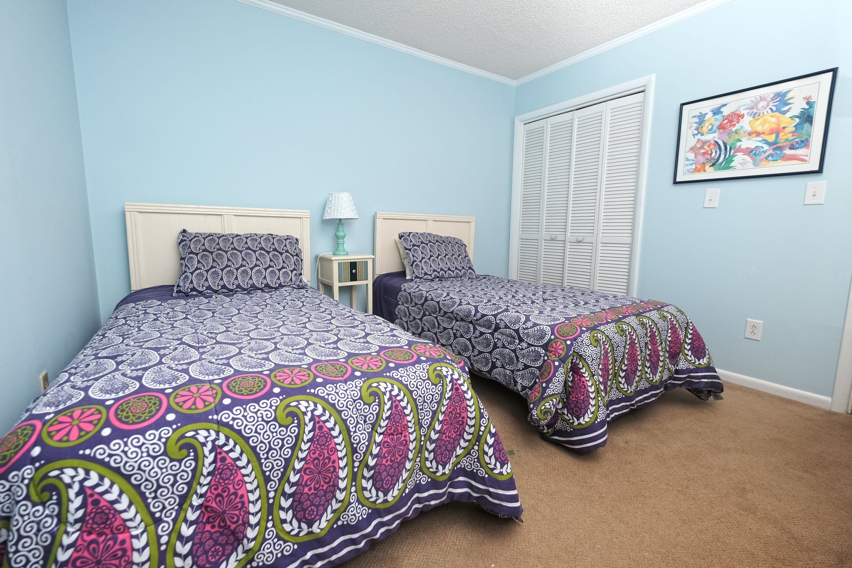 Un dormitorio con dos camas, cada una con ropa de cama estampada, una mesita de noche con lámpara y una ventana con persianas.