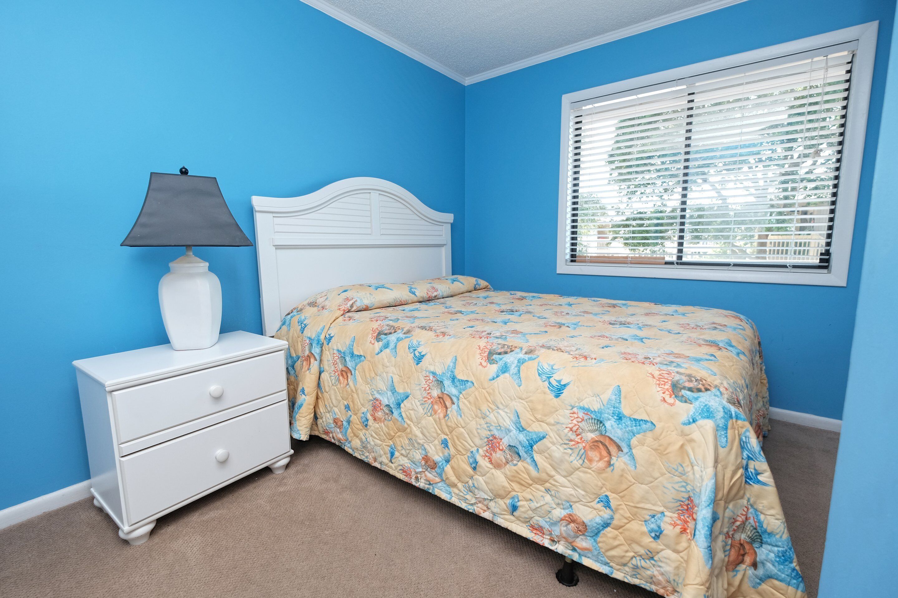 Une chambre à coucher avec un lit, une table de chevet, une lampe et une fenêtre avec des stores.