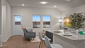 A modern kitchen with a granite countertop, a dining area with a gray sofa and chairs, and a view through the windows. - Marbella Lane - Amazing 4BR Lakeview Home (Austin)