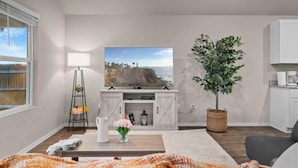 A modern living room with a flat-screen TV, a dining table, a potted plant, and a white cabinet. - Marbella Lane - Amazing 4BR Lakeview Home (Austin)