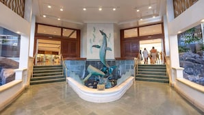 A lobby with a central sculpture of a whale, a staircase, and a view of the entrance. - Marbella Lane - Ocean Marina View Ilikai Hotel (Honolulu)