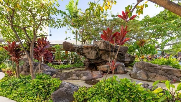 A landscaped garden with large rocks, various plants, and a tree with red leaves. - Marbella Lane - Ocean Marina View Ilikai Hotel (Honolulu)