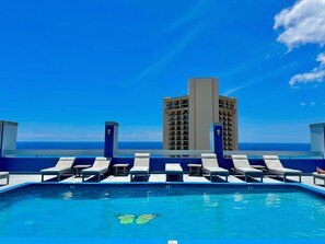 A pool with lounge chairs and a view of a tall building. - Newly Innovated Oceanview Beach Condo Sauna Pool (Honolulu)