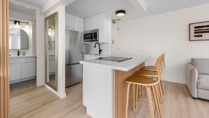 Een moderne keuken met witte kasten, een roestvrijstalen koelkast en een magnetron. Er is een klein eiland met een spoelbak en krukken.