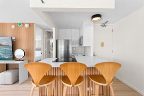 Cozinha moderna com armários brancos, geladeira de aço inoxidável e uma ilha central com bancada preta. Três cadeiras de madeira com design exclusivo.