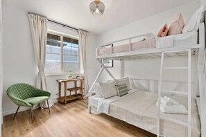 A bunk bed room with a green chair, a small table, and a window with curtains. - Marbella Lane - Serene & Lovely MT Ocean Views (Waianae)