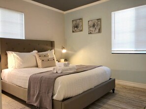A bedroom with a large bed, a nightstand with a lamp, and two wall-mounted flower paintings.