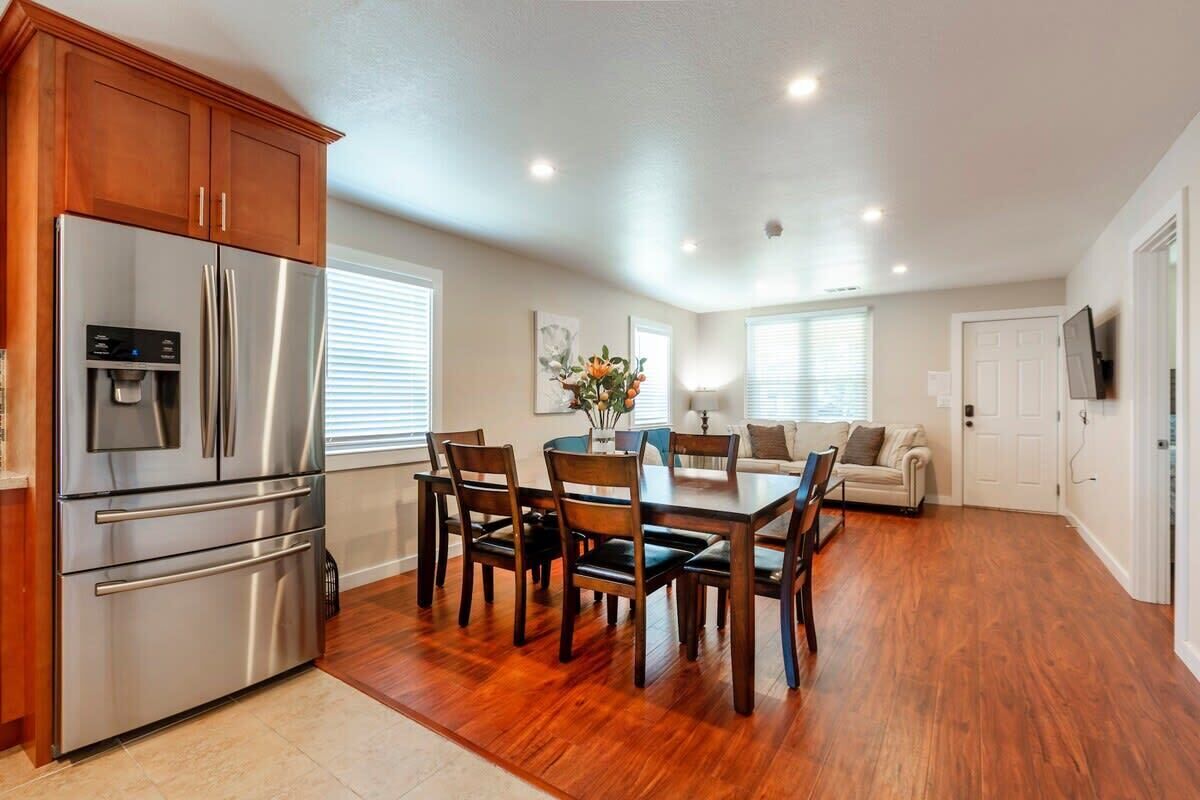 A modern kitchen with a stainless steel refrigerator, wooden cabinets, and a dining area with a wooden table and chairs.