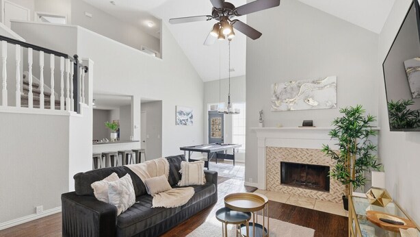 A modern living room with a black sofa, a fireplace, a ceiling fan, and a dining area in the background. - Luxe 3B 5B Cozy, Spacious Home, 5-star Stay in Frisco (Frisco)