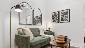 A green sofa, a floor lamp, and two framed floral artworks on the wall. - 2BR 2BA in Historic Brownstone Near Subway (New York)