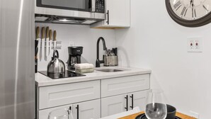 A modern kitchen with a stainless steel refrigerator, a microwave, a kettle, a coffee maker, and a sink with a faucet. There is a clock on the wall and a wine glass on the counter. - 2BR 2BA in Historic Brownstone Near Subway (New York)