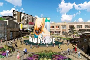Uma praça pública com um grande outdoor, edifícios modernos e pessoas caminhando.