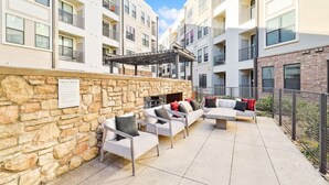 A modern outdoor patio with stone walls, wicker furniture, and a fire pit. - Luxurious 2b2b Near Toyota HQ, The Star, Legacy West (Frisco)