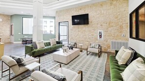 A spacious living area with a stone wall, a flat-screen TV, and a green sofa. - Luxurious 2b2b Near Toyota HQ, The Star, Legacy West (Frisco)
