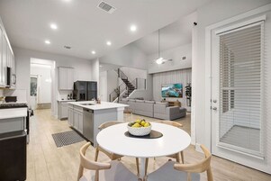 A modern kitchen with a central island, a dining area with a round table, and a living room with a sofa and TV.