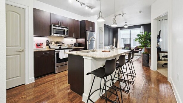 Una cocina moderna con armarios oscuros, electrodomésticos de acero inoxidable y una isla central con taburetes de bar.