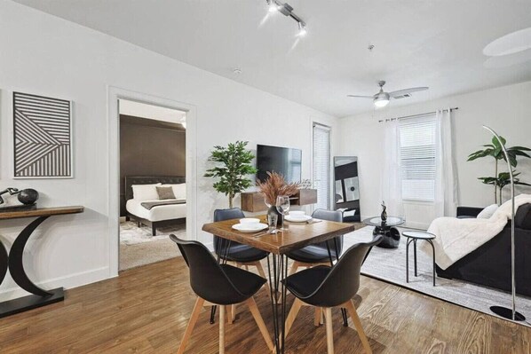 A modern living room with a dining area, a sofa, a coffee table, and a TV. - Chic and Stylish 2B Near Legacy West Wi-fi (Frisco)