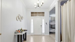 A hallway with a white door, a small table with decorative items, a chandelier, and a view into a room with bunk beds. - Bright & Cozy 4BR Home w Movie Room & Backyard (Frisco)