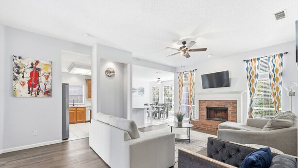 A modern living room with a fireplace, a dining area, and a kitchen. - Bright & Cozy 4BR Home w Movie Room & Backyard (Frisco)