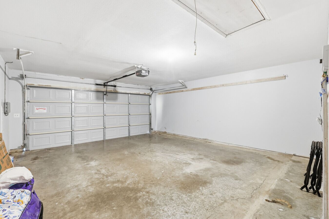 Un garage avec une porte blanche, un projecteur fixé au plafond et un sol en béton.
