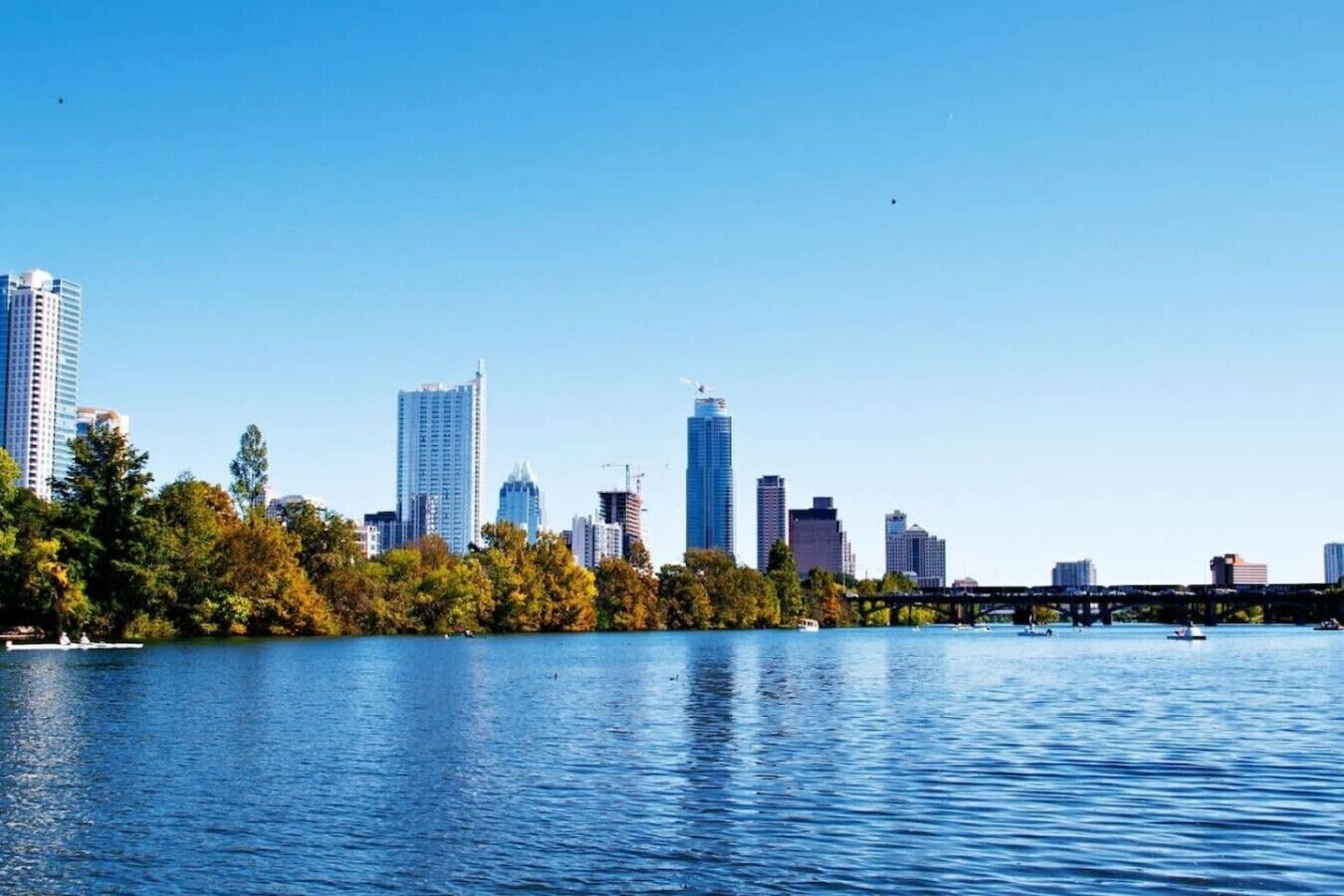 Un horizonte urbano con edificios modernos y altos, una masa de agua y un puente.